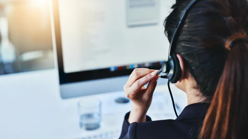 Woman wearing headset working at a computer, providing customer support in an office environment.