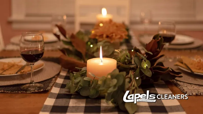 Cozy dinner table setup with lit candles, wine glasses, greenery centerpiece, and warm ambient lighting.