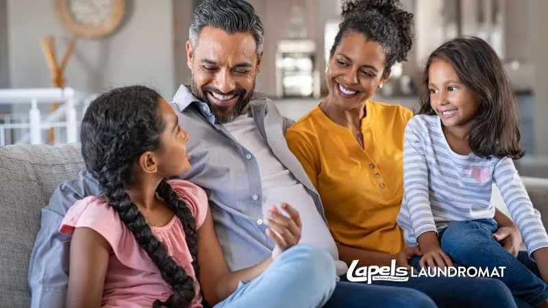 Happy family with two daughters sitting on a couch and smiling in a cozy living room setting.