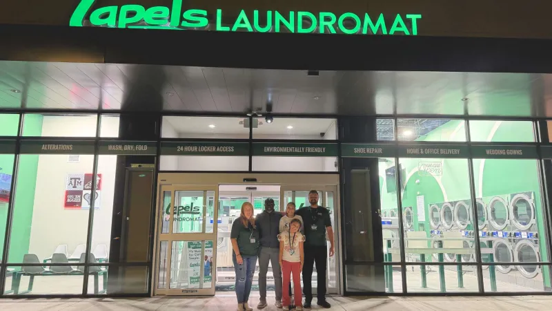 Four people standing outside Lapels Laundromat with green signage and washing machines visible inside at night
