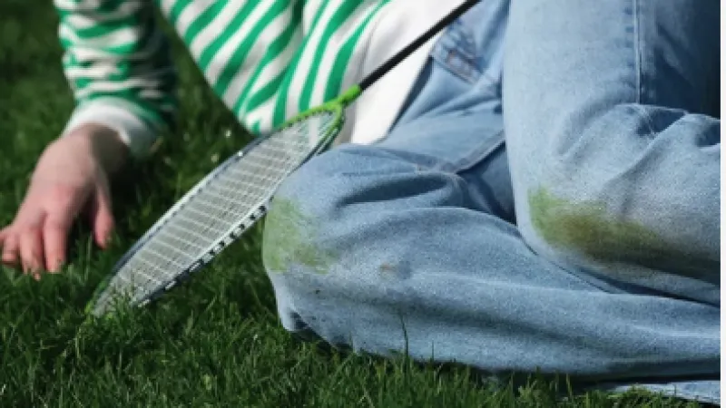 Person in striped shirt and jeans with grass stains lying on green grass holding badminton racket