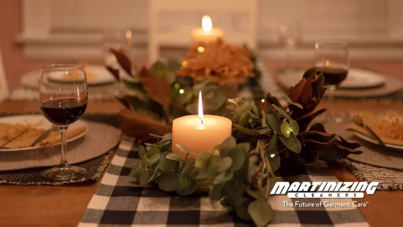 Cozy dinner table with lit candle centerpiece, greenery, wine glasses, and warm ambient lighting for intimate dining.