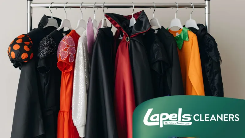 Variety of colorful costumes and garments hanging on a rack against a white wall with Lapels Cleaners logo.