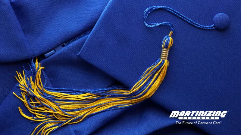 Blue graduation cap with gold and blue tassel lying on matching blue gown fabric.