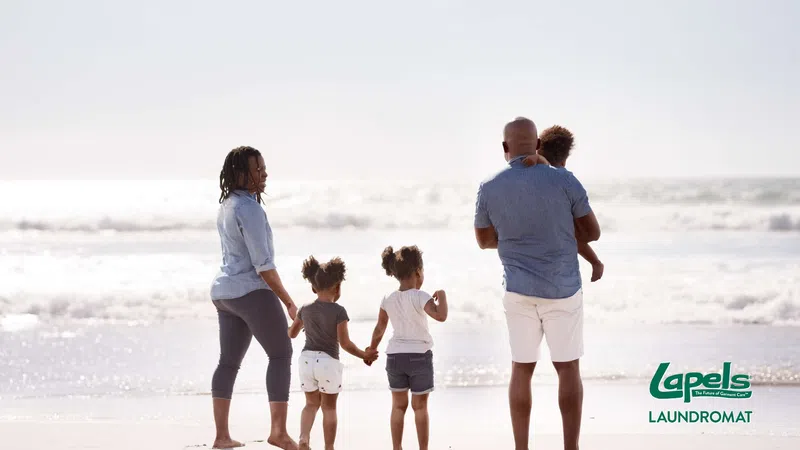 Family of five walking on the beach at sunset with ocean waves in the background and Lapels Laundromat logo.