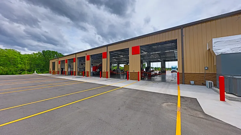 Modern auto repair shop with multiple service bays and empty parking lot under a cloudy sky.