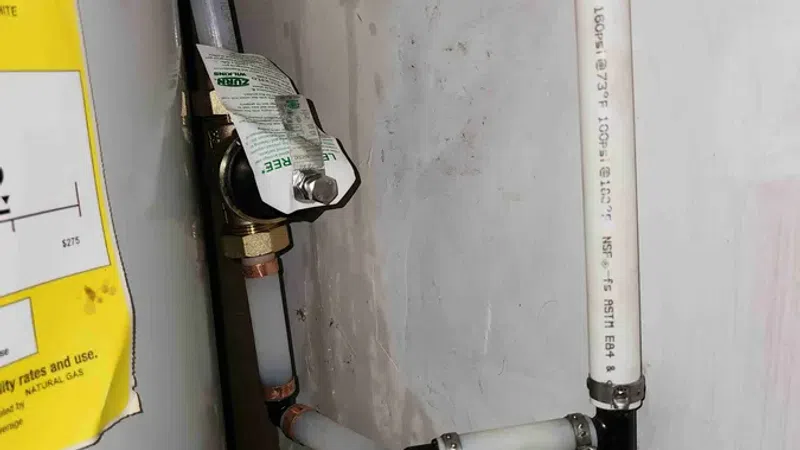 White and copper plumbing pipes with valves and connectors attached to a wall beside a water heater.