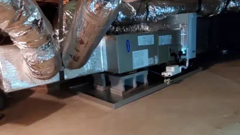 Insulated HVAC ductwork and unit installed in a basement or crawl space with tools on the floor.
