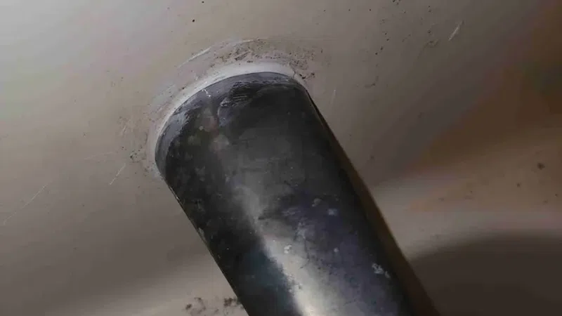 Close-up of a black bathtub spout with signs of wear and grime on surrounding white surface.
