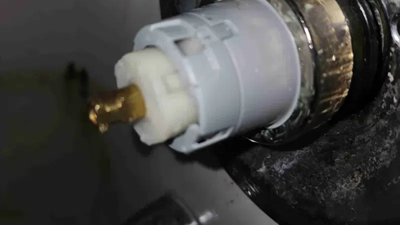 Close-up of a faucet valve stem with worn brass and plastic components in a bathroom sink fixture.