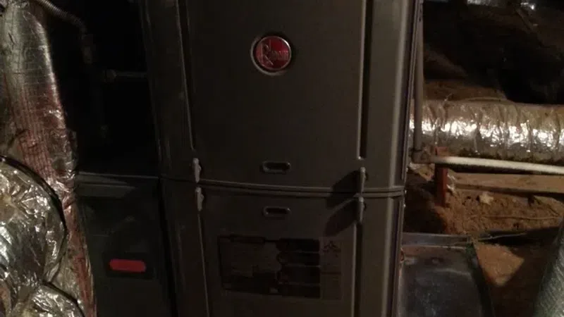 Old metal furnace unit installed in basement with insulated ductwork and ventilation pipes