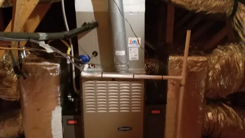 Installed Carrier furnace with metal ducts and insulated air vents in an attic space with wooden beams.