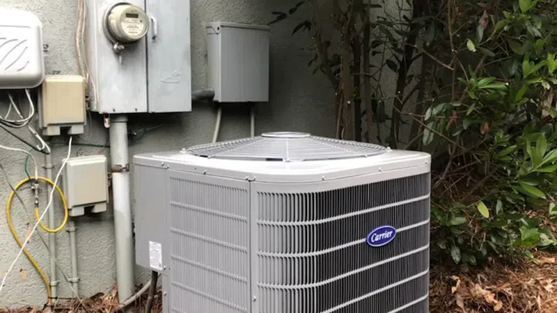 Carrier air conditioning unit installed outside near electrical boxes and green shrubbery.