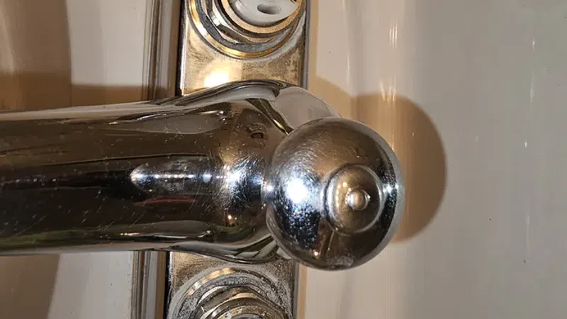Close-up of a bathtub faucet with the handles removed showing valve stems and chrome finish.