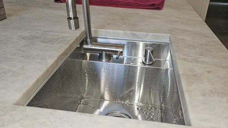 Modern stainless steel kitchen sink with a curved faucet set into a light countertop with a red towel nearby.