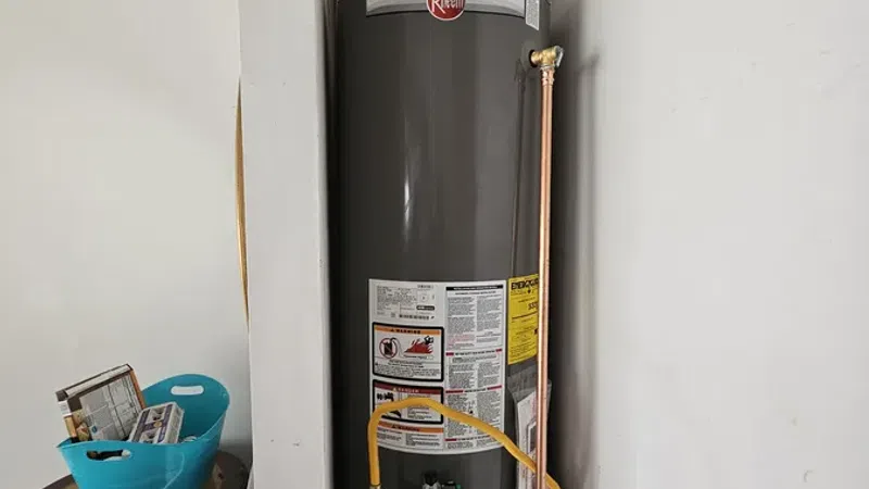 Tall Rheem water heater installed in a home utility closet with connected copper and gas pipes.