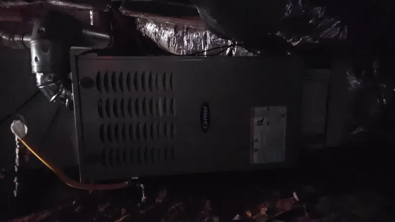 Carrier HVAC unit installed in a dimly lit crawl space with ventilation ducts and piping.