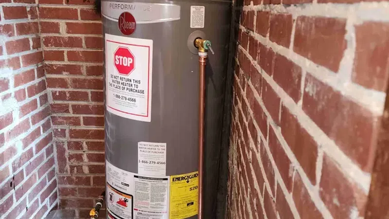 Tall gray Rheem water heater installed in narrow brick-walled utility space with copper piping and warning labels.