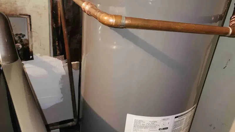Gray Rheem water heater tank with copper and yellow gas pipes installed in a utility room.