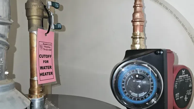 Close-up of water heater pipes with cutoff valve tag and timer control device attached to copper plumbing.