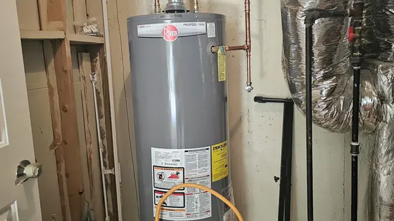 Gray Rheem water heater installed in basement with copper pipes and ventilation duct, surrounded by insulation and concrete walls.