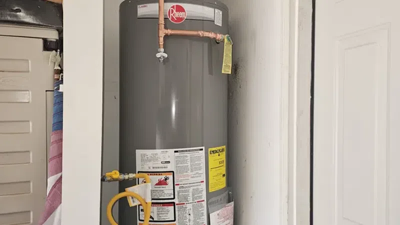 Gray Rheem water heater installed in a small utility closet with copper plumbing and gas valve connections.