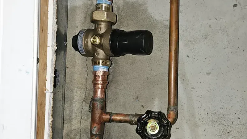 Copper plumbing pipes with two valve handles and a pressure regulator installed inside a wall opening.