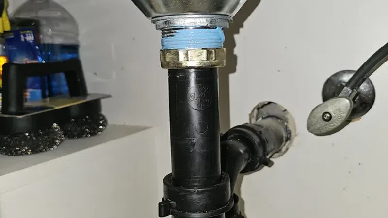 Under-sink plumbing with black PVC pipe trap and metal sink drain fitting in a utility area.