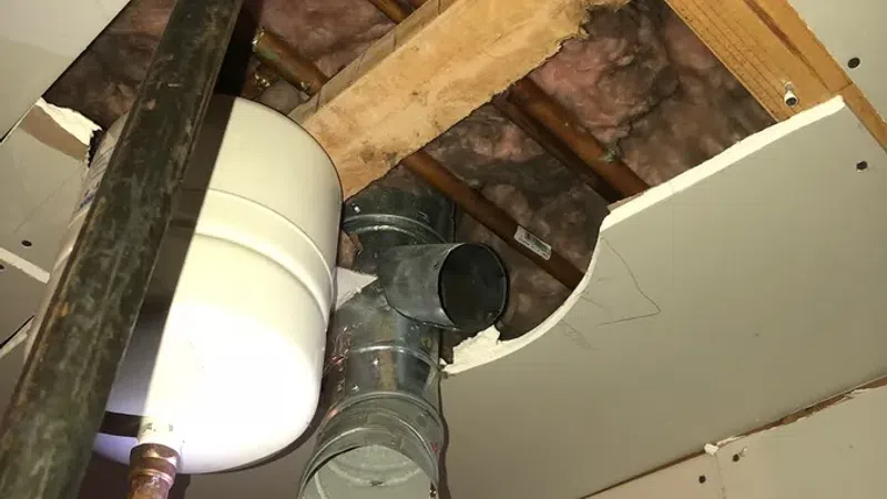 Exposed ceiling pipes and ductwork with insulation and drywall partially removed in a maintenance area