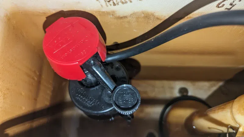 Close-up of a toilet tank's internal mechanism with a red-flush valve handle and visible water level.