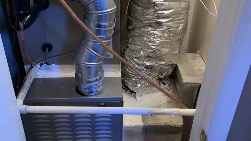 Indoor Carrier brand HVAC furnace with connected ductwork and insulated pipe in a utility closet.