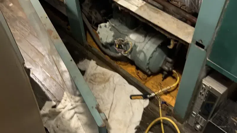 Industrial HVAC unit maintenance area with exposed machinery, tools, and yellow air hose on wooden floor.
