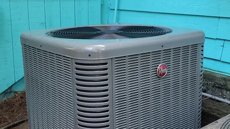 Gray Rheem outdoor air conditioning unit installed beside a turquoise wooden house exterior.
