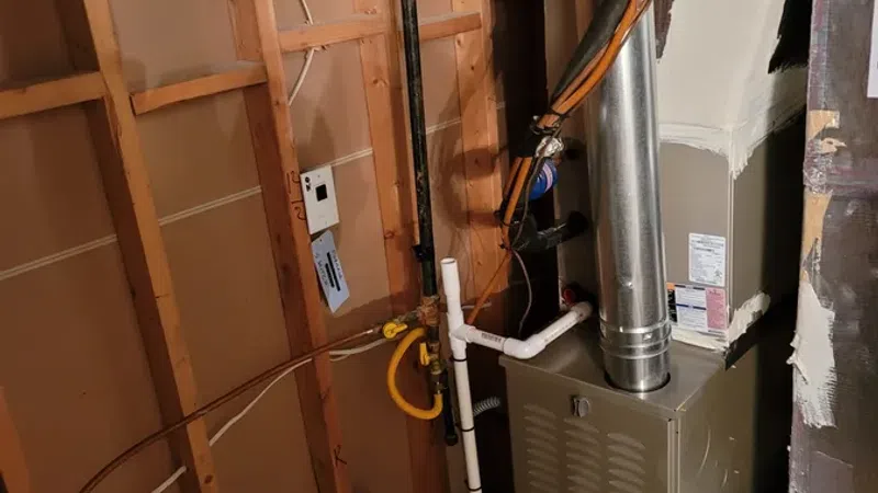Residential furnace and ductwork installed in unfinished basement with exposed wooden framing.
