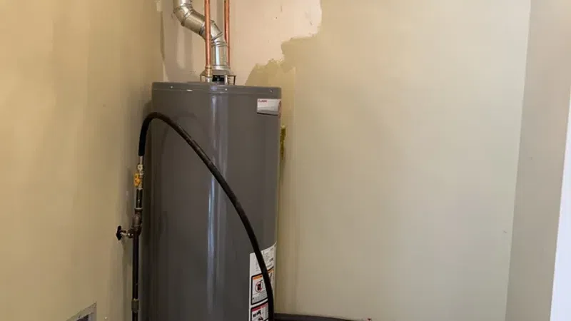 Gray water heater installed in a small utility room with connected pipes and an expansion tank.