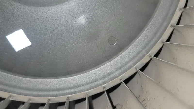 Close-up of a dusty metal fan blade and inner hub with a bolt in an industrial setting.