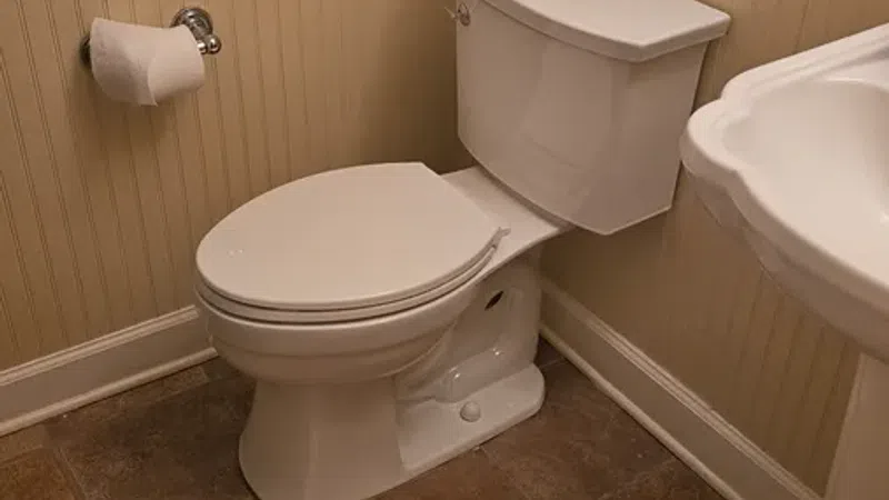 Small beige bathroom featuring a white toilet, towel rack with towel, toilet paper holder, and pedestal sink.