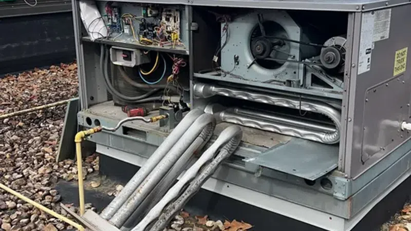 Open rooftop HVAC unit showing internal components and connected insulated pipes on a gravel roof.