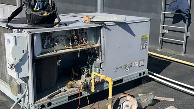 Open rooftop HVAC unit with exposed wiring and tools, undergoing maintenance or repair under clear sky.