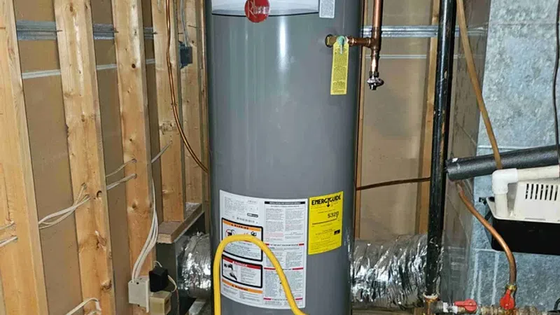 Gray Rheem water heater installed in a utility room with exposed wooden framing and metal ductwork.
