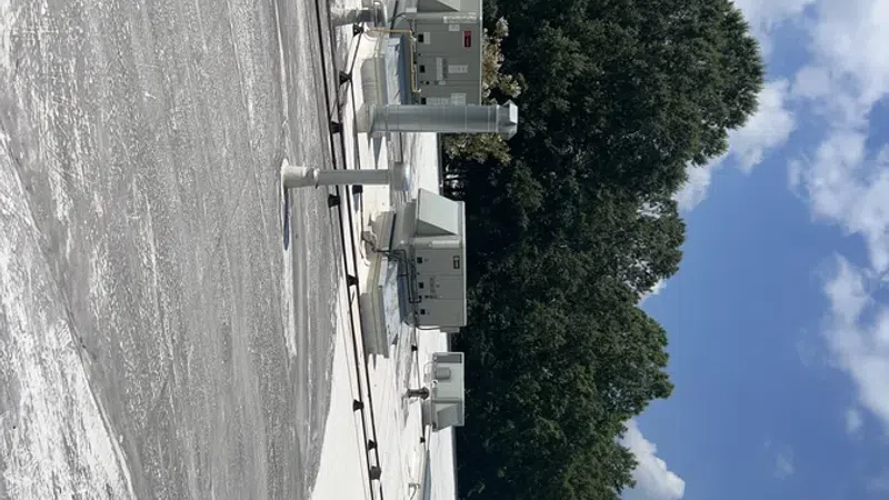 Rooftop with HVAC units and vents under a partly cloudy sky and green trees in the background