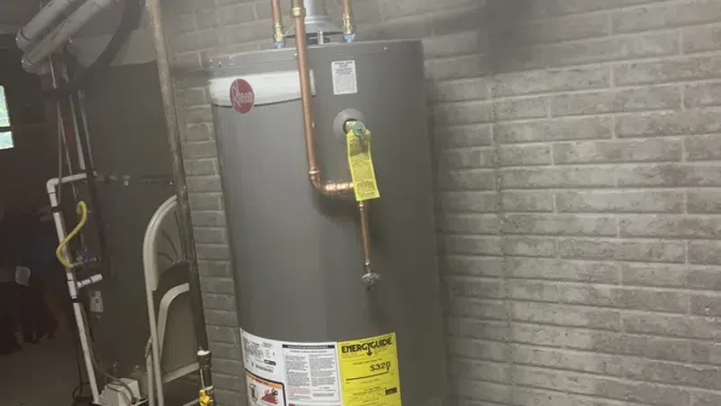 Gray Rheem water heater installed in basement with copper piping and expansion tank mounted above.