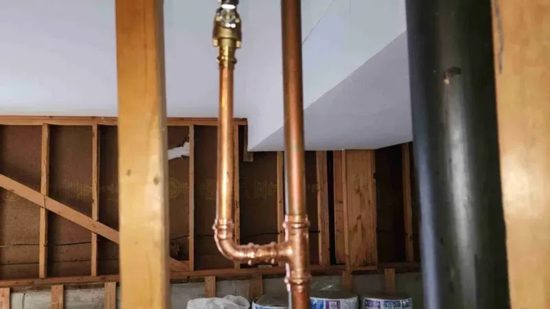 Copper plumbing pipes installed inside wooden frame walls in an unfinished basement with insulation materials on the floor.