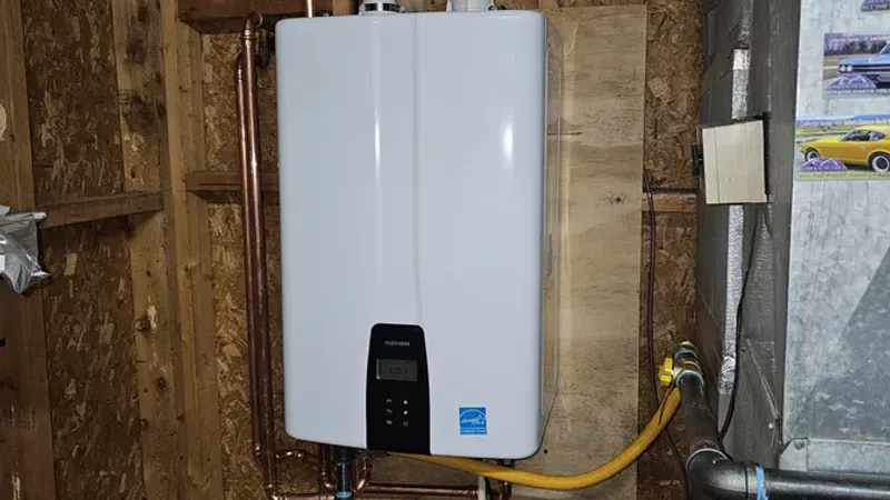 Modern white tankless water heater installed on wooden wall with copper pipes and ventilation ducts.