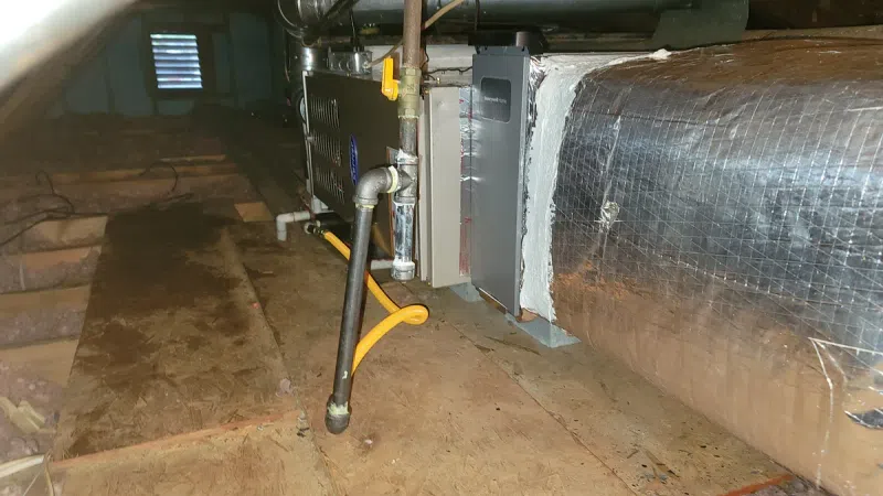 HVAC unit and ductwork installed in a wooden attic space with exposed pipes and insulation.