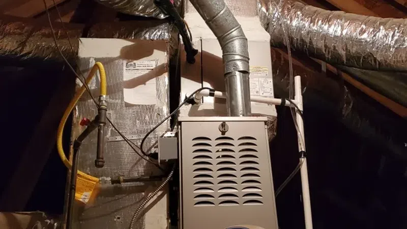 Carrier HVAC furnace system installed in an attic with insulated ductwork and metal vent pipes under wooden beams.