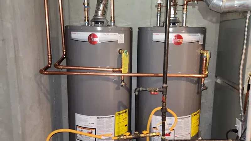 Two gray residential water heaters with copper and yellow gas pipes installed in a basement unit.