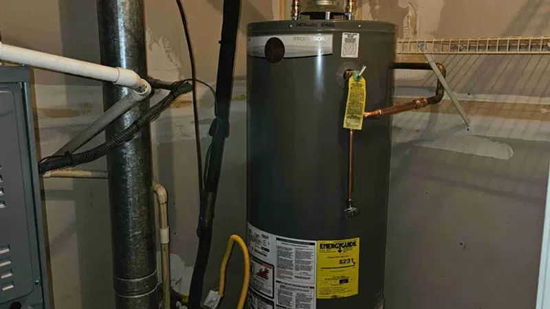 Gray water heater with connected pipes in a basement utility room with concrete floor and wire shelves.