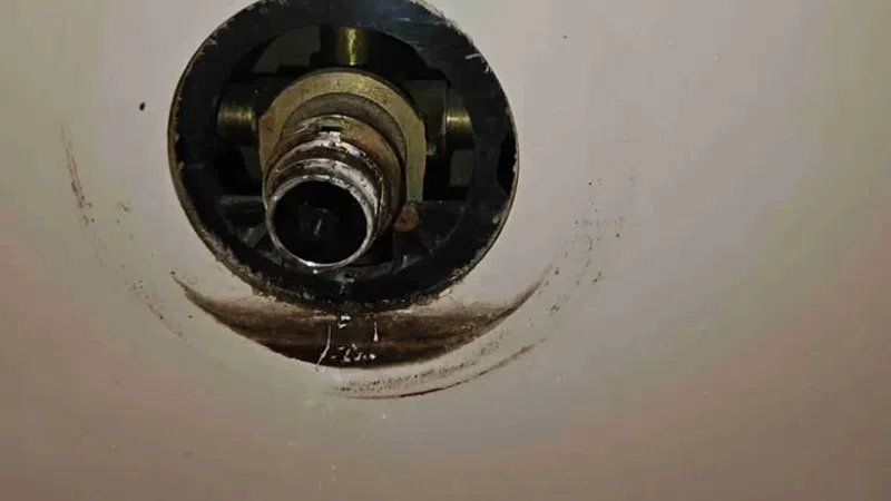 Close-up of a shower valve with a missing handle and visible water droplets inside a white bathtub.