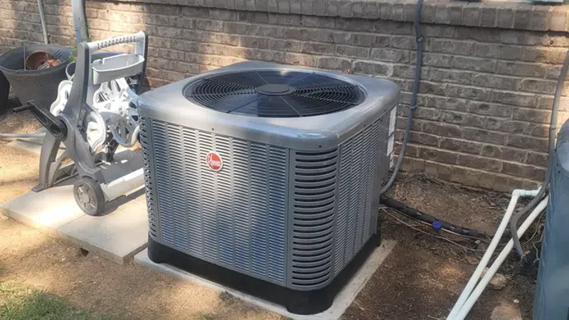 Modern outdoor HVAC unit installed next to a brick wall on a concrete pad with surrounding grass and pipes.